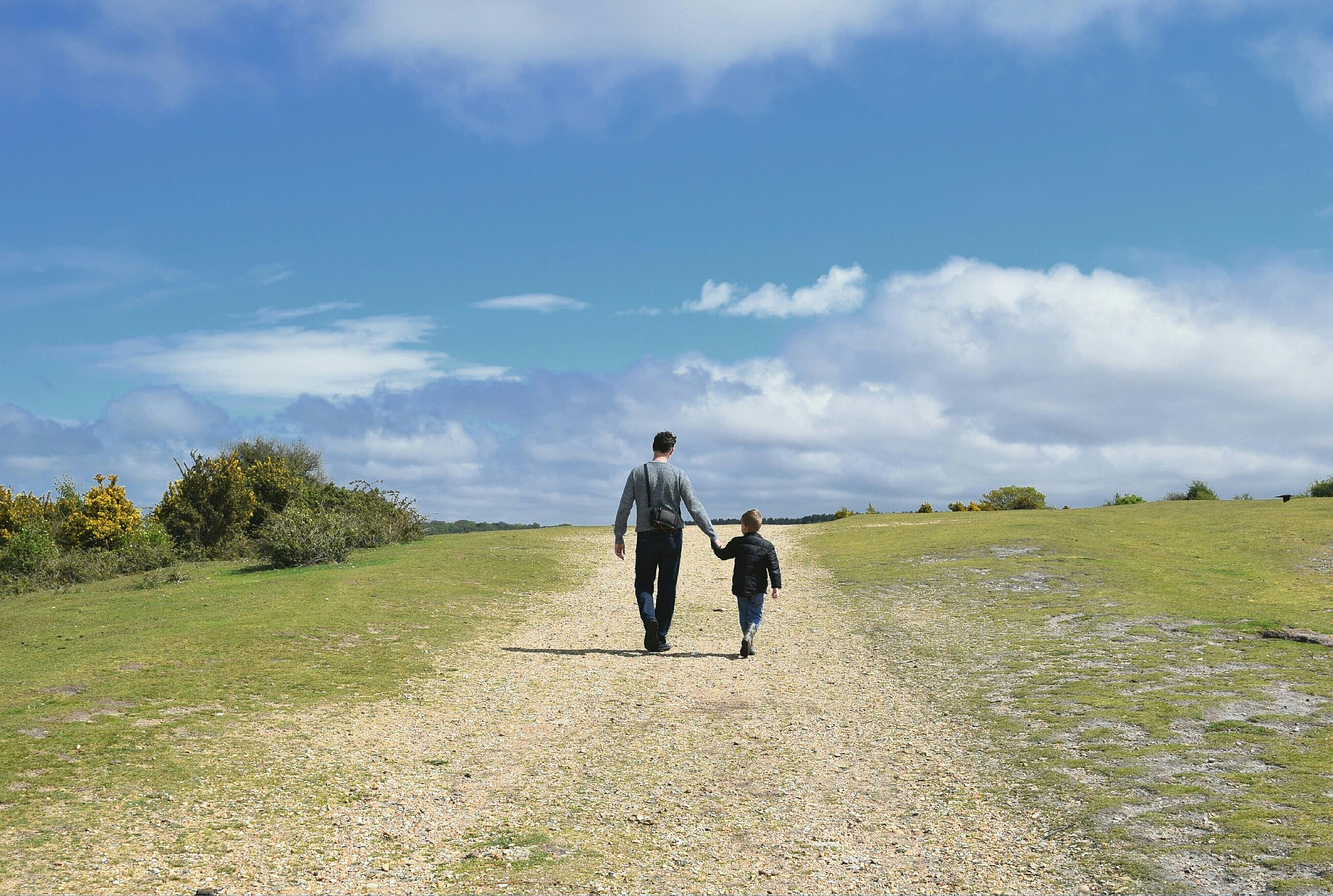 Father walking and holding the hand of a child down a dirt road